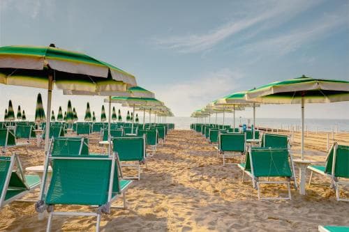 A serene beach scene features rows of green lounge chairs and striped umbrellas under a clear sky, ideal for a relaxing seaside getaway.