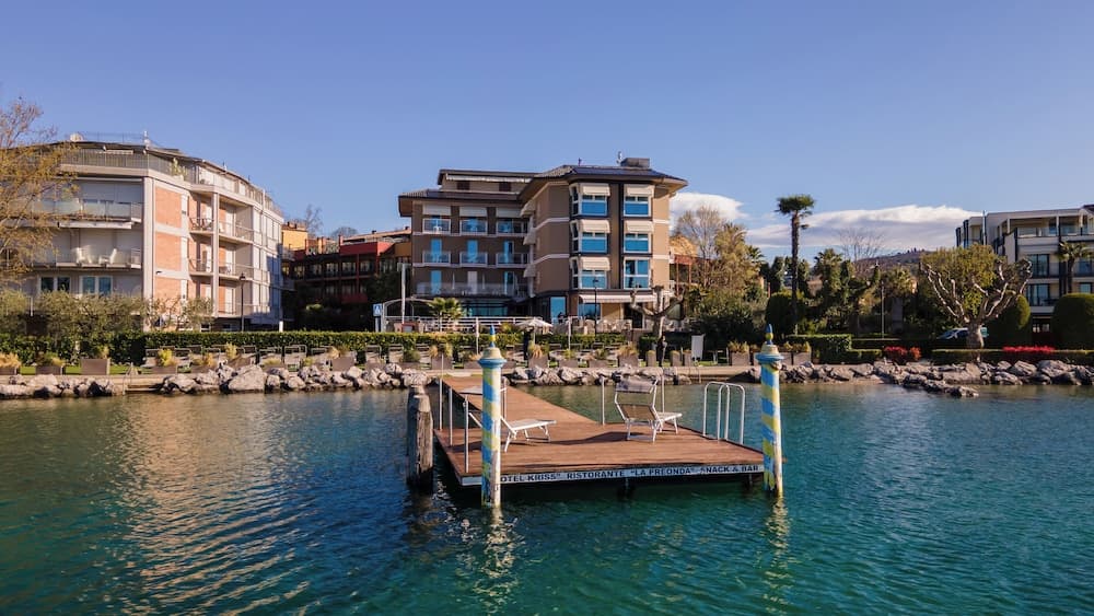 A serene waterfront scene features a dock leading to a modern hotel complex surrounded by lush greenery, ideal for travelers seeking relaxation and leisure activities near the water.