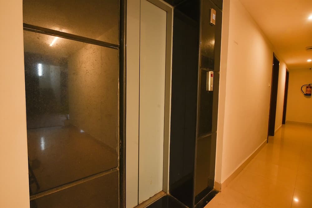 A warmly lit hotel corridor features an elevator with mirrored doors, a fire extinguisher on the wall, and a quiet ambiance ideal for travelers seeking a peaceful stay.