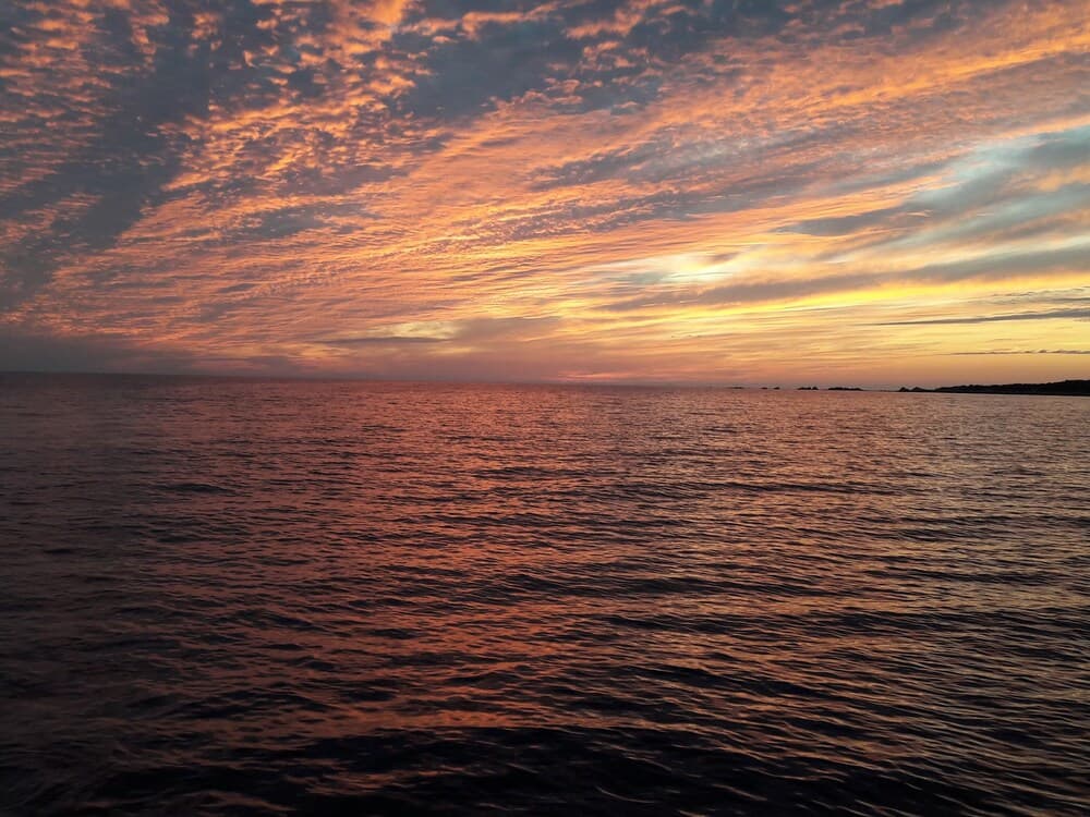 A serene ocean at sunset showcases vibrant orange and pink hues in the sky, reflecting on calm waters, ideal for tranquil beachside relaxation or photography enthusiasts.
