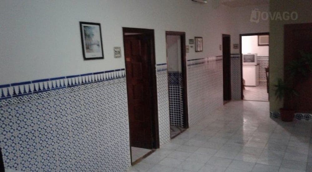 A cozy hotel corridor adorned with blue and white tiled walls, framed artwork, and wooden doors creates a welcoming atmosphere ideal for travelers seeking a charming accommodation experience.