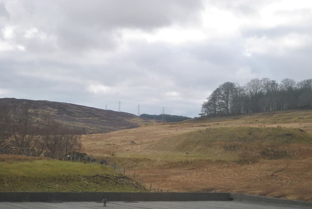A serene rural landscape featuring rolling hills, sparse trees, and distant power lines under a cloudy sky, ideal for tranquil countryside exploration and photography.