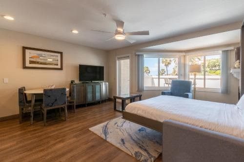 A cozy beachside studio apartment features a spacious layout with a king bed, dining area, and large windows offering serene ocean views, ideal for a relaxing coastal getaway.