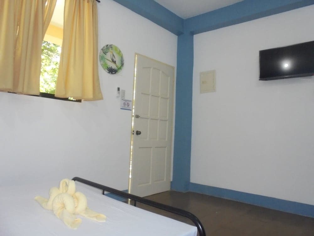 A cozy hotel room with blue accents, yellow curtains framing a sunny window view, a neatly folded towel on the bed, and a mounted TV, ideal for travelers seeking comfort and simplicity.