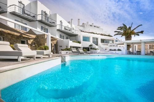 A serene luxury resort features a crystal-clear pool surrounded by white sun loungers and modern architecture, ideal for a relaxing vacation getaway.