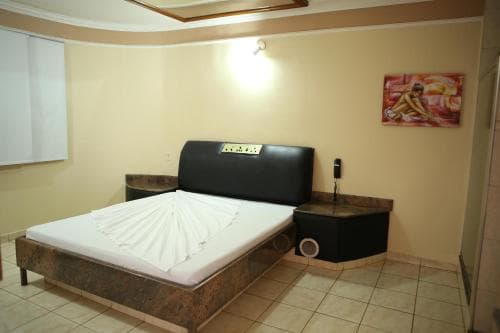 A cozy hotel room features a neatly made bed with a decorative white spread, a sleek black bedside unit with a speaker, warm lighting, and a vibrant wall art piece, ideal for travelers seeking comfort and relaxation.