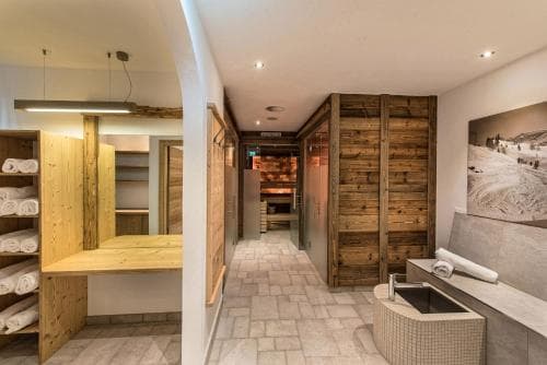 A cozy spa area featuring wooden sauna doors, tiled floors, neatly stacked towels, and a modern sink, ideal for relaxation and wellness retreats.