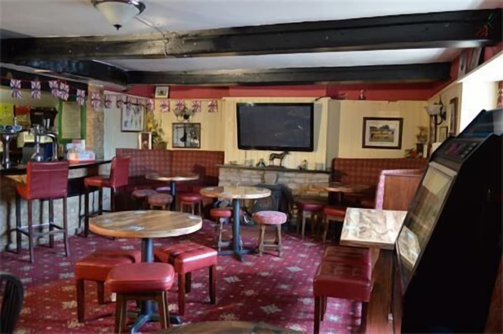 A cozy traditional pub interior features wooden tables, red upholstered seating, Union Jack flags, and a warm ambiance, ideal for travelers seeking a classic British drinking experience.