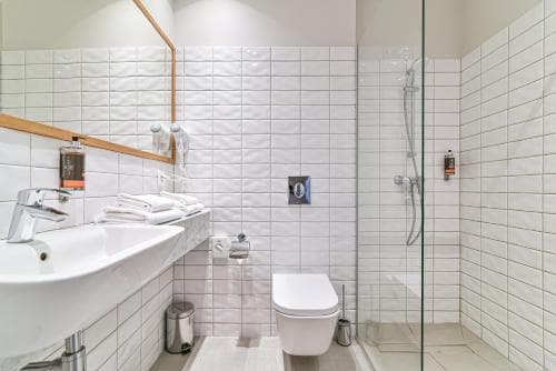 A modern, minimalist bathroom with white tiled walls, a sleek sink, a glass-enclosed shower, and neatly folded towels creates a clean and serene atmosphere ideal for travelers seeking comfort in accommodations.