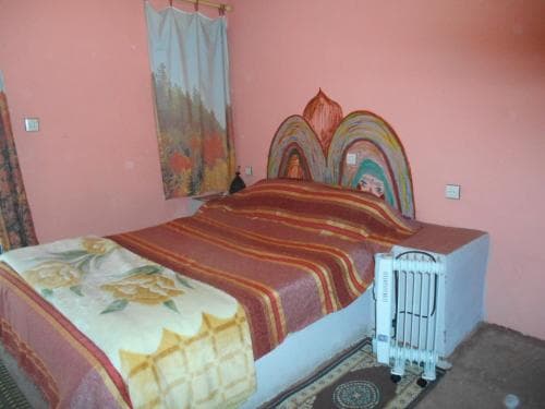 A cozy bedroom with pink walls, a floral-patterned bedspread, and a painted headboard offers a warm and inviting atmosphere, ideal for travelers seeking a comfortable and budget-friendly accommodation.