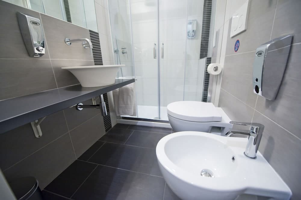 A modern, sleek bathroom with gray tiles, dual sinks, a glass-enclosed shower, and stainless steel fixtures offers a clean and functional space ideal for travelers seeking comfort in accommodations.