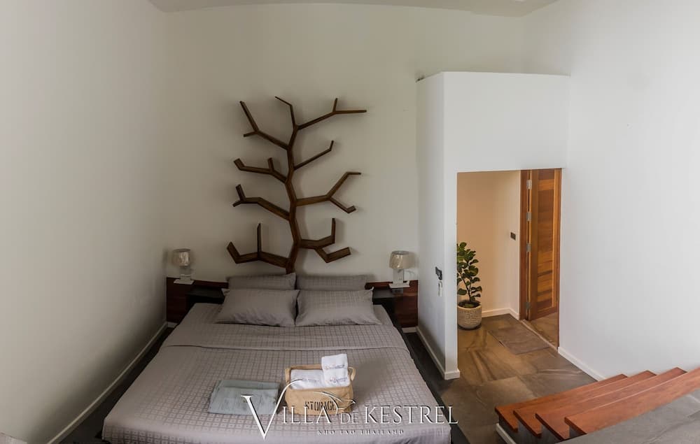A serene minimalist bedroom with a tree-shaped wall decoration, wooden accents, and a cozy bed setup invites travelers seeking relaxation in a modern retreat.