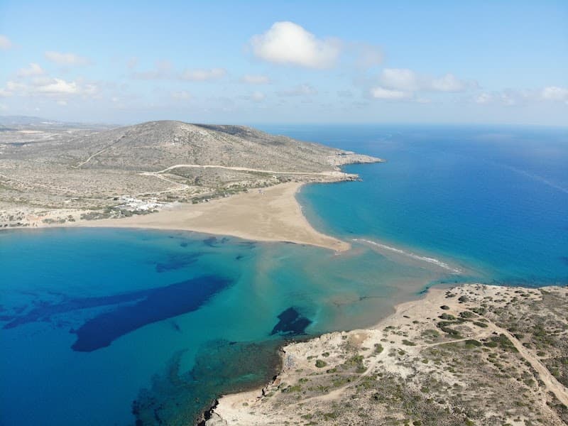 A breathtaking aerial view of Prasonisi's serene sandy beach nestled between turquoise waters and rugged hills, ideal for adventure seekers exploring Greece's natural beauty.