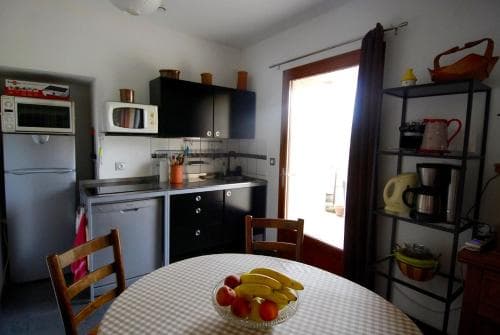 A cozy kitchen with a round table set with fresh fruit, featuring modern appliances and a bright doorway leading to natural light, ideal for travelers seeking a comfortable self-catering stay.
