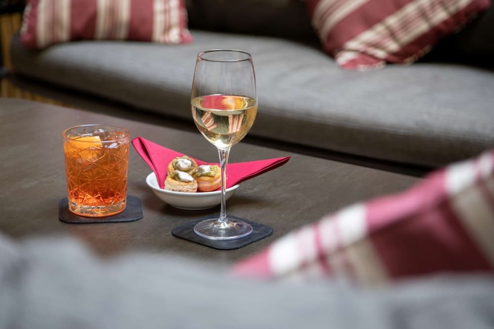 A cozy living room scene featuring a glass of white wine, an orange cocktail, and appetizers on a coffee table, evoking a relaxed and inviting atmosphere perfect for intimate gatherings or leisurely evenings at home.