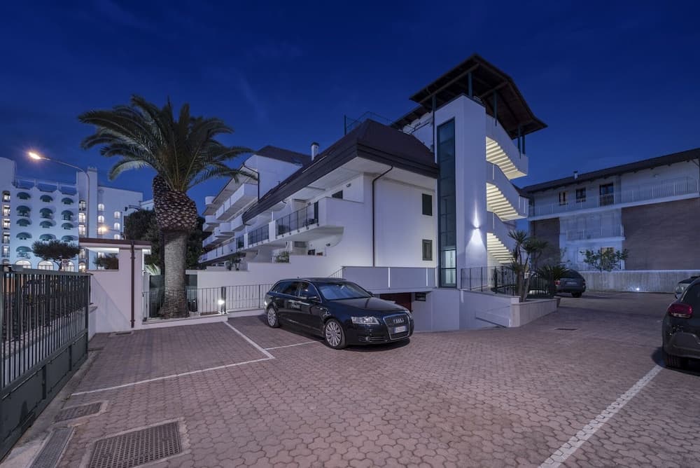 A serene evening view of a modern residential complex with illuminated balconies, palm trees, and parked cars, ideal for travelers seeking a tranquil urban retreat.