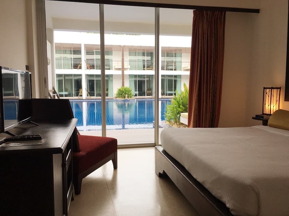 A serene hotel room with a cozy bed, flat-screen TV, and sliding glass doors leading to a tranquil poolside view, perfect for a relaxing vacation getaway.