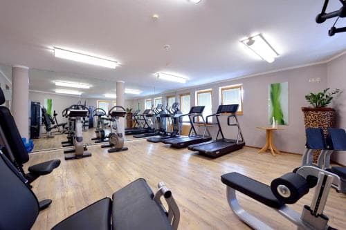 A well-lit indoor fitness center with wooden floors, treadmills, weight machines, and large mirrors creates an inviting atmosphere for travelers seeking exercise during their stay.