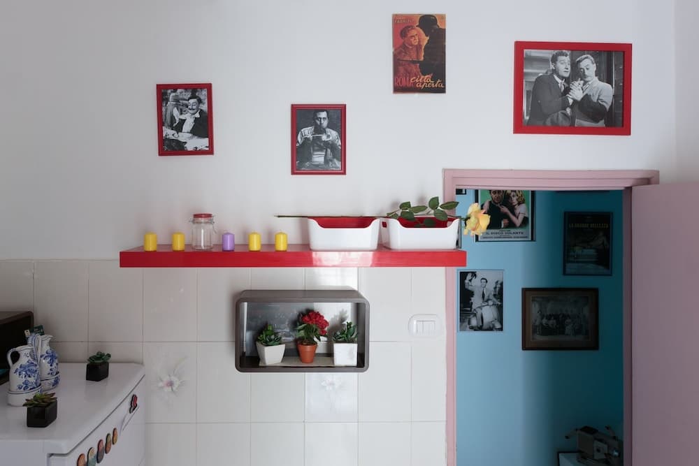 A cozy kitchen corner adorned with framed black-and-white movie posters, colorful candles on a red shelf, and potted plants, evokes a nostalgic and artistic ambiance ideal for travelers seeking unique cultural experiences.