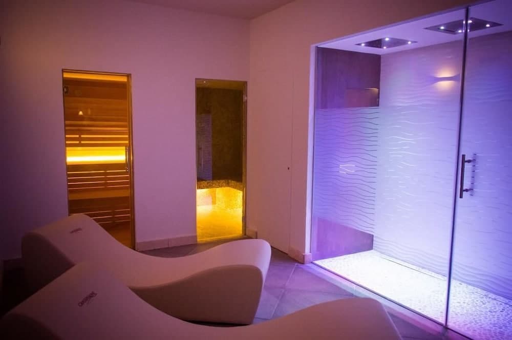A serene spa relaxation room features modern lounge chairs, glowing sauna and steam room entrances, and ambient purple lighting, ideal for travelers seeking rejuvenation and wellness experiences.