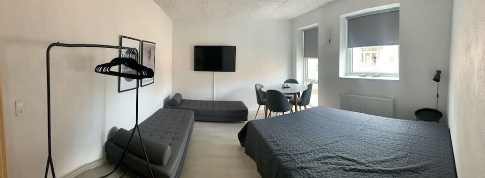 A cozy studio apartment features a neatly made bed, a tufted sofa, a dining area by the window, and modern decor, ideal for travelers seeking comfort and convenience in an urban setting.