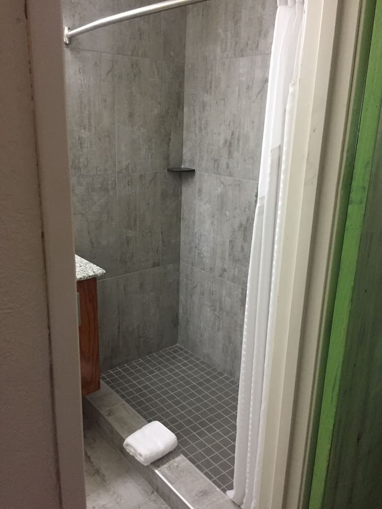 A cozy hotel bathroom features a modern gray-tiled shower with a white towel on the step, ideal for travelers seeking comfort and cleanliness.