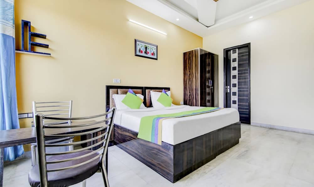 A cozy hotel room with a neatly made bed adorned with colorful pillows, a small dining area, wooden furniture, and soft yellow walls creates a welcoming atmosphere ideal for travelers seeking comfort and relaxation.