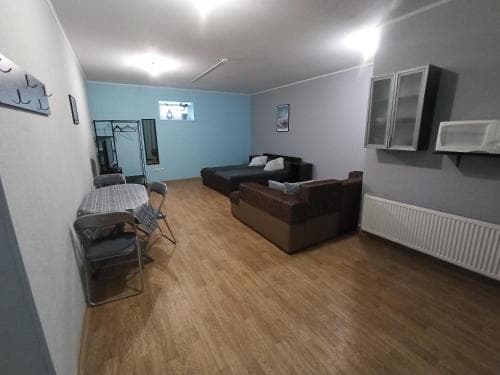 A cozy apartment living room with wooden flooring, comfortable sofas, a dining area, and modern decor offers an inviting space for travelers seeking a homey stay.