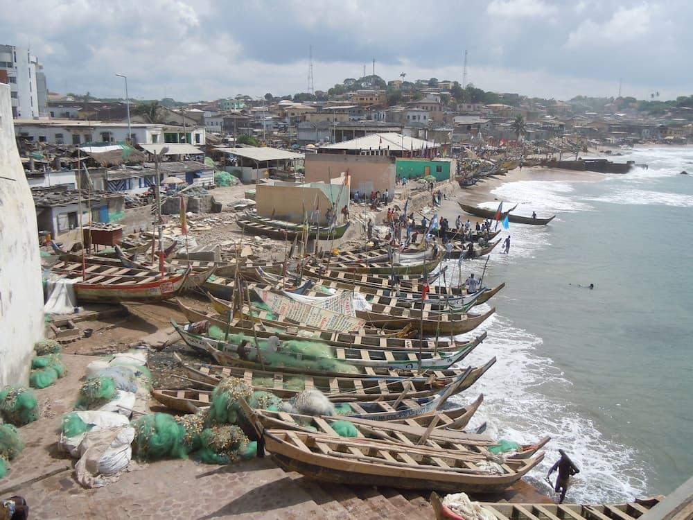 A bustling coastal fishing village scene with wooden boats lined up on the shore, vibrant nets, and a lively community atmosphere, ideal for cultural exploration and photography.