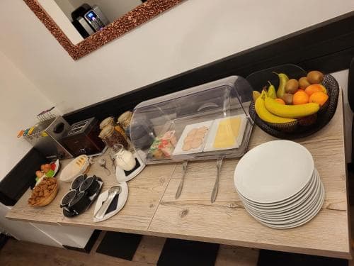 A cozy hotel breakfast nook features a wooden table set with fresh fruits, pastries, and neatly stacked plates, creating an inviting atmosphere for travelers seeking a convenient morning meal.