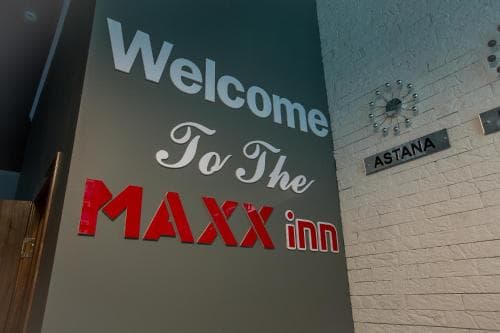 A warmly lit hotel lobby welcomes travelers to the MAXX inn in Astana, featuring modern decor and a clock-adorned wall, ideal for business or leisure stays.