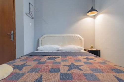 A cozy bedroom with a neatly made bed adorned in a star-patterned quilt, illuminated by a warm hanging lamp, ideal for travelers seeking a comfortable and inviting accommodation.