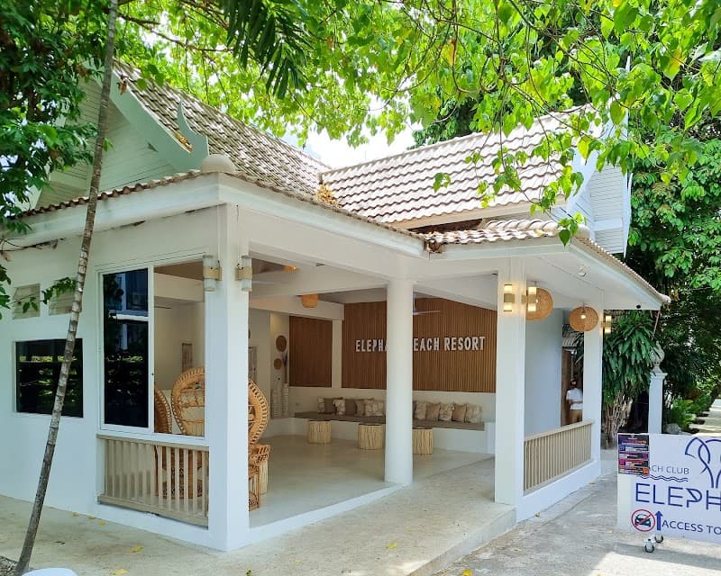 A serene tropical resort entrance at Elephant Beach Club & Resort Samui features a cozy seating area under lush greenery, ideal for travelers seeking relaxation and luxury on Chaweng Beach Road.