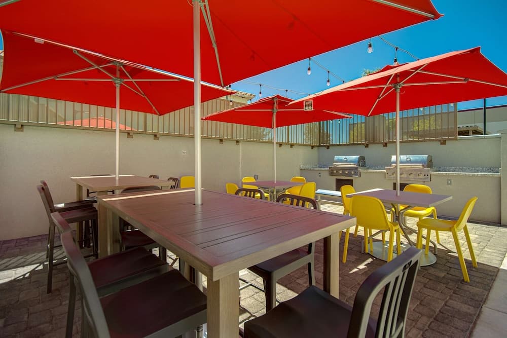 A vibrant rooftop patio features wooden tables under bold red umbrellas, paired with colorful chairs, ideal for outdoor dining or social gatherings in sunny weather.