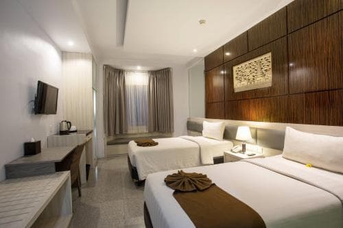 A cozy hotel room features two neatly made beds with decorative throws, modern wooden furnishings, and soft lighting, creating a welcoming atmosphere ideal for travelers seeking comfort and relaxation.