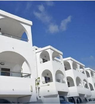 A serene coastal resort features pristine white buildings with arched balconies under a clear blue sky, ideal for travelers seeking relaxation and picturesque accommodations.