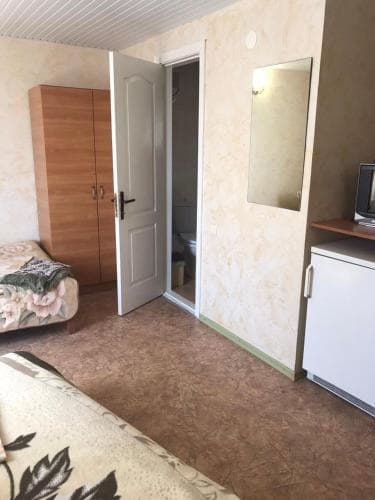 A cozy hotel room with floral-patterned bedding, a wooden wardrobe, a mirror on the wall, and an open door leading to a bathroom, ideal for travelers seeking a simple and functional accommodation.