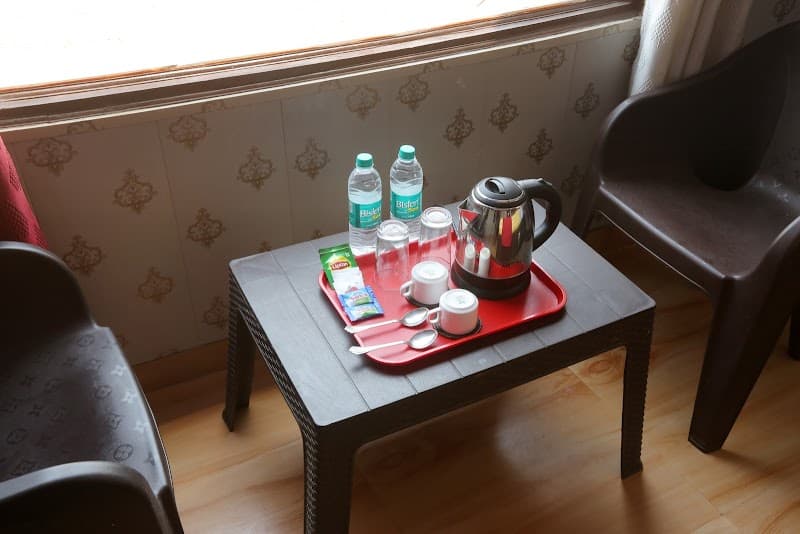 A cozy corner in a hotel room at Jhansi Castle Inn features a small table with tea-making essentials, water bottles, and cups, set against patterned wallpaper, ideal for travelers seeking comfort and convenience.