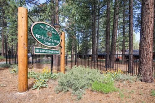 A serene forest entrance marked by a wooden signpost for the Recreation & Swim Complex invites travelers to explore its tranquil, tree-lined grounds ideal for outdoor activities.
