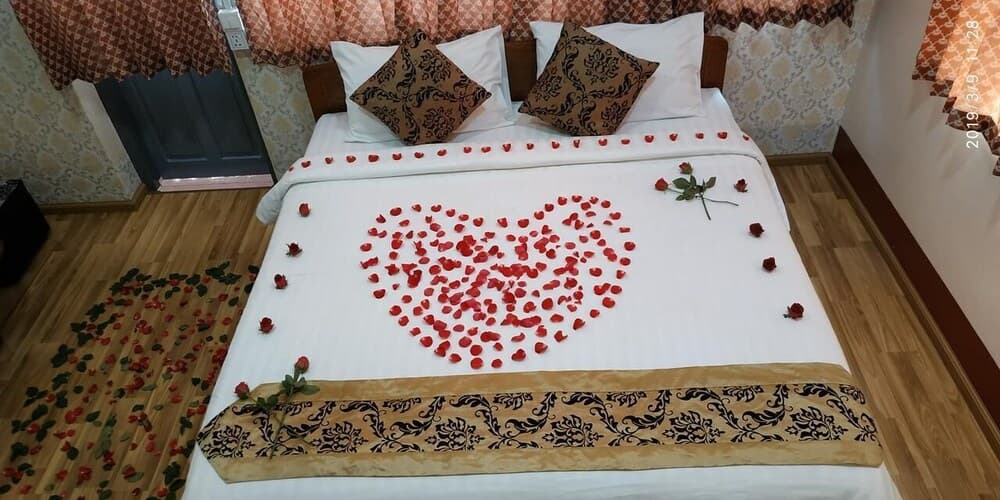 A cozy hotel room features a bed adorned with a heart-shaped arrangement of red rose petals, creating a romantic atmosphere ideal for honeymooners or couples seeking a special getaway.