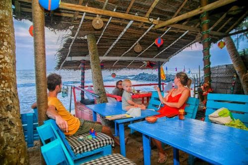 A vibrant beachside hut with wooden beams and colorful tables offers a relaxed seaside dining experience, perfect for travelers seeking a casual tropical getaway.
