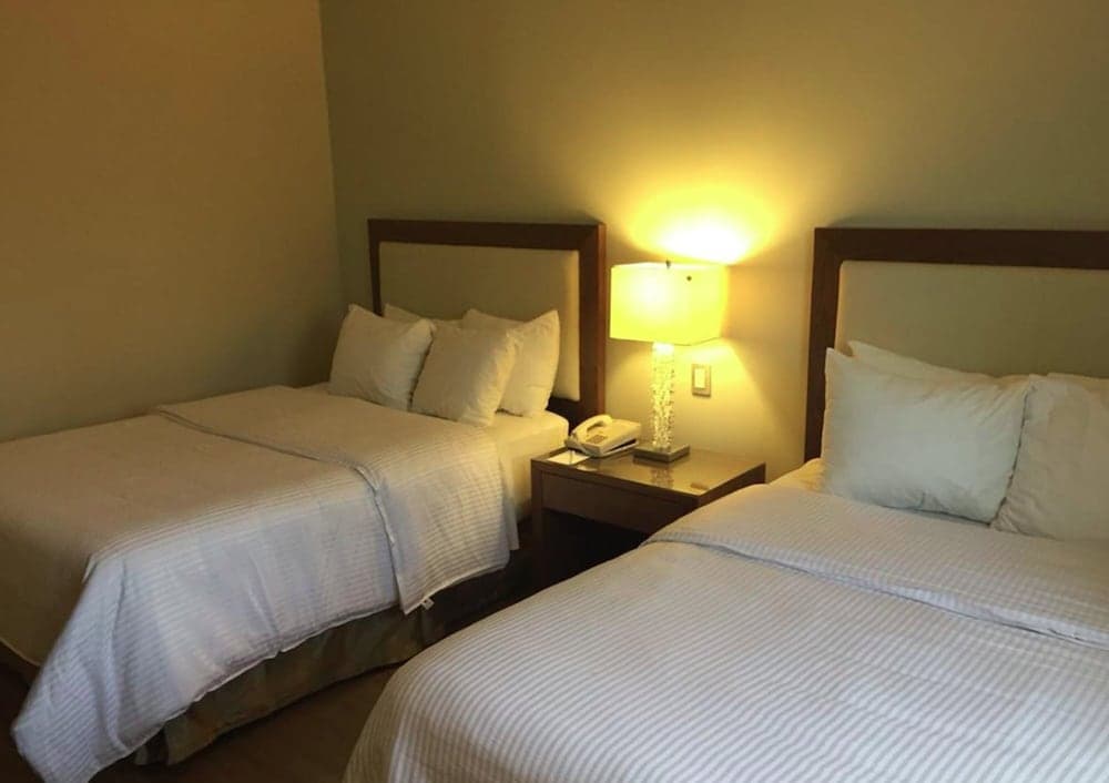 A cozy hotel room with two neatly made beds, a glowing bedside lamp, and a warm ambiance is ideal for travelers seeking comfort and relaxation.