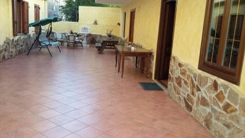 A cozy outdoor patio with tiled flooring, rustic stone walls, wooden furniture, and a green umbrella offers a serene retreat for travelers seeking relaxation in a quaint countryside setting.
