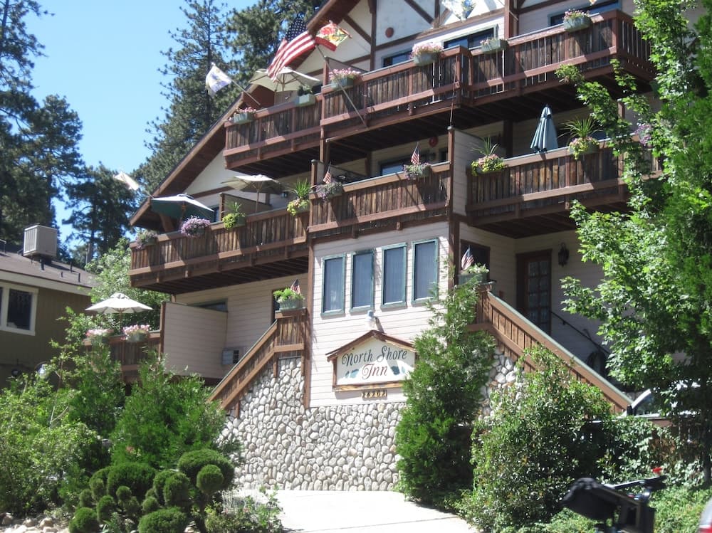 A charming multi-story inn adorned with balconies, flags, and lush greenery offers a cozy retreat in a serene forested area, ideal for travelers seeking a peaceful getaway.