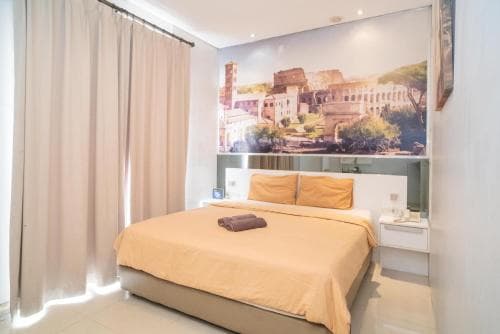 A cozy hotel room features a neatly made bed adorned with orange bedding, a large wall mural of ancient ruins, soft curtains, and modern furnishings, ideal for travelers seeking comfort and cultural ambiance.