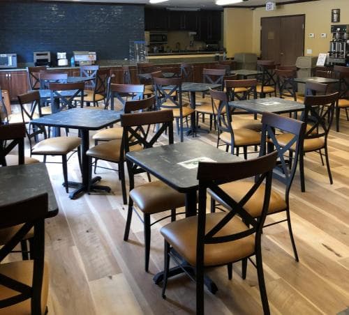 A cozy café with wooden floors, black tables, and cushioned chairs invites travelers to relax and enjoy a quiet moment over coffee or a meal.