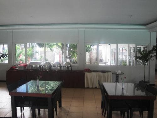 A cozy indoor dining area with tiled floors, wooden tables, and large windows offering a view of greenery outside, ideal for travelers seeking a relaxed meal in a casual restaurant setting.