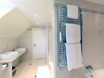 A bright, modern bathroom with white tiled walls, a towel radiator, dual sinks, and natural light from a skylight, ideal for travelers seeking cleanliness and comfort in their accommodations.
