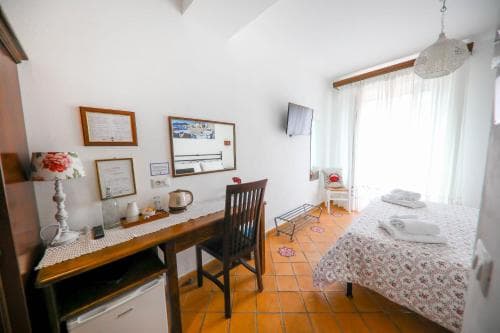 A cozy guesthouse room features a tiled floor, wooden furniture, and bright natural light from sheer curtains, creating an inviting atmosphere ideal for travelers seeking comfort and simplicity.
