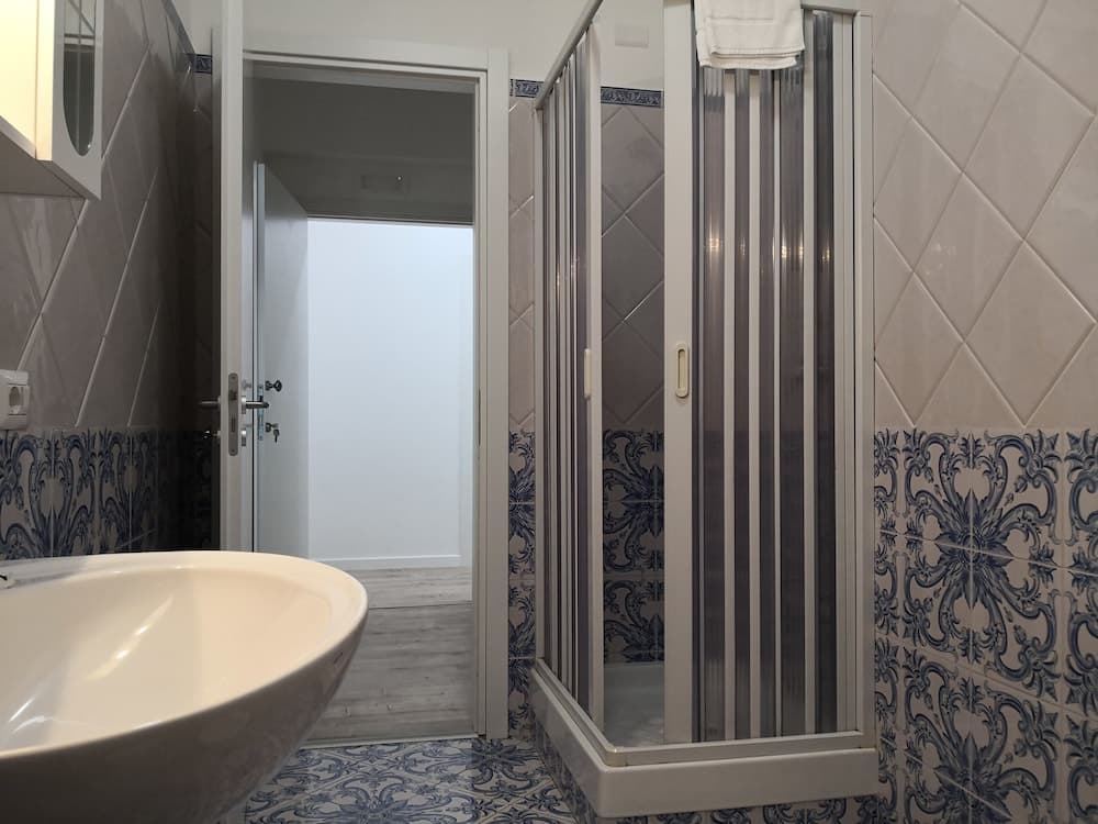 A modern bathroom with elegant blue and white patterned tiles, a sleek glass shower enclosure, and a stylish sink creates a serene and luxurious atmosphere ideal for travelers seeking comfort and design in their accommodations.